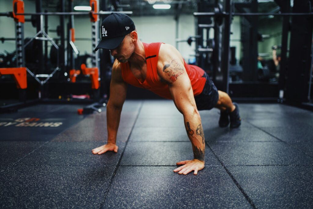 man in red tank top and black shorts doing push up on the street